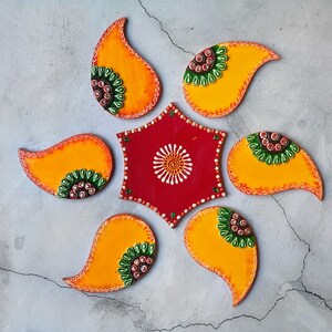 May include: A set of seven decorative wall hangings in the shape of teardrop-shaped paisley designs. The hangings are made of wood and painted in shades of orange, yellow, green, and red. The centre piece is a star-shaped design with a red background and white accents.