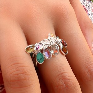 May include: A silver ring with a cluster of colorful gemstones. The ring features a variety of oval-shaped stones, including green, purple, red, and yellow.