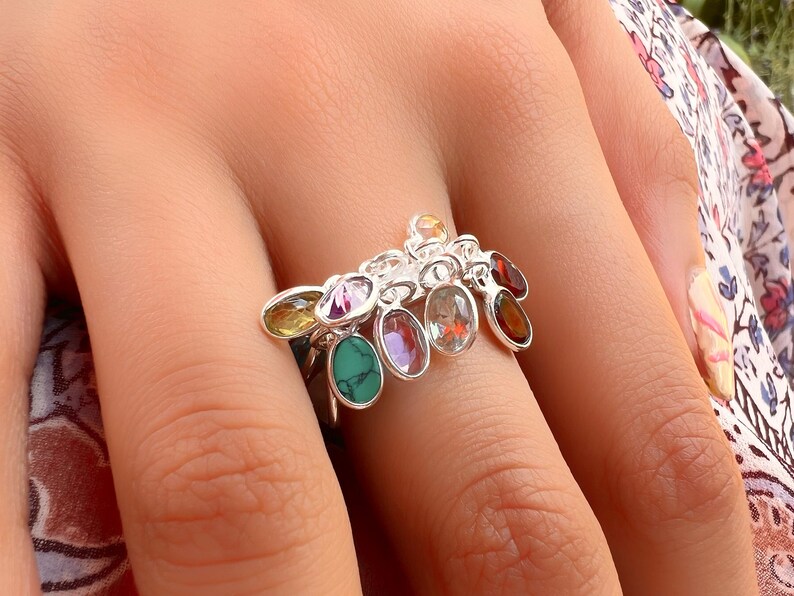 May include: A silver ring with a cluster of colorful gemstones. The ring features a variety of oval-shaped stones, including green, purple, red, and yellow.