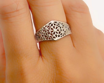 Puede incluir: Un anillo de plata con un delicado diseño floral. El anillo se lleva en un dedo.