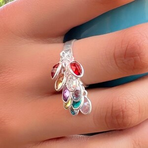May include: A silver ring with a cascading design of colorful gemstones. The ring features a variety of colors, including red, orange, yellow, green, blue, purple, and clear.