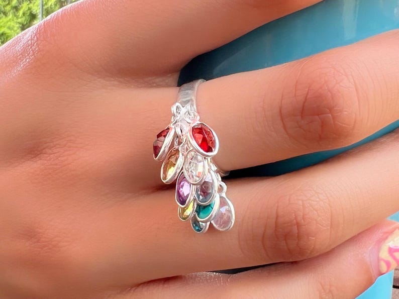 May include: A silver ring with a cascading design of colorful gemstones. The ring features a variety of colors, including red, orange, yellow, green, blue, purple, and clear.