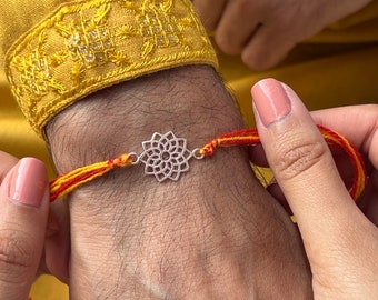 May include: A red and yellow thread bracelet with a silver mandala charm. The bracelet is tied around a person's wrist.