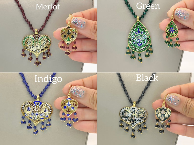 May include: Four sets of gold necklaces and earrings with enamel pendants. The pendants are in the shape of a heart and a teardrop. The necklaces are on a maroon, blue, green, and black background. The earrings are on a hand.
