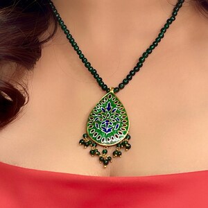 May include: A green and blue enamel pendant necklace with a teardrop shape and intricate floral design. The necklace is made of gold and has a green beaded chain.