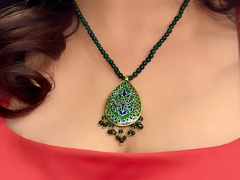 May include: A green and blue enamel pendant necklace with a teardrop shape and intricate floral design. The necklace is made of gold and has a green beaded chain.