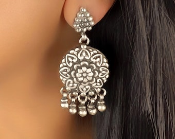 May include: Silver dangle earrings with a round, ornate, floral design and a cluster of small, round beads hanging from the bottom.