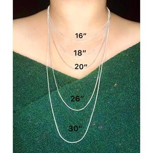 Pode incluir: Cinco correntes de prata de diferentes comprimentos, 16 polegadas, 18 polegadas, 20 polegadas, 26 polegadas e 30 polegadas, são mostradas no pescoço de uma pessoa.