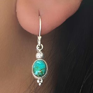 May include: Silver dangle earrings with a turquoise stone and a silver bead.