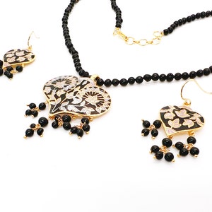 May include: A black beaded necklace with a gold heart-shaped pendant featuring a floral design. The pendant is accented with black beads. Matching earrings with a similar design are included.