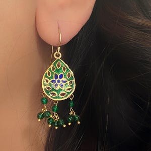 May include: Gold dangle earrings with a green and blue enamel teardrop pendant and green bead accents.