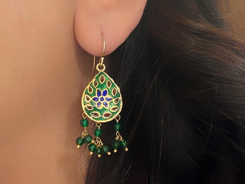 May include: Gold dangle earrings with a green and blue enamel teardrop pendant and green bead accents.