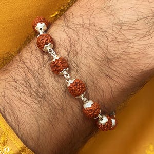 Könnte beinhalten: Ein braunes und silbernes Armband mit runden Perlen. Das Armband wird am Handgelenk einer Person getragen.