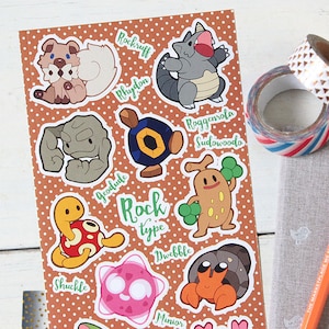 May include: A sheet of stickers featuring various Pokemon characters from the Rock type. The stickers are on a brown background with white polka dots. The Pokemon characters include Rockruff, Rhydon, Geodude, Sudowoodo, Shuckle, Dwebble, Minior, Tyranitar, and Corsola.