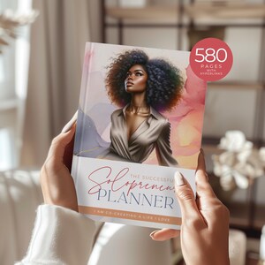 May include: A book cover with a woman with dark brown skin and curly black hair. The book cover is a watercolor design with pink, blue, and purple hues. The title of the book is "The Successful Solopreneur Planner" and the subtitle is "I am co-creating a life I love". The book cover also includes the text "580 Pages with Hyperlinks".