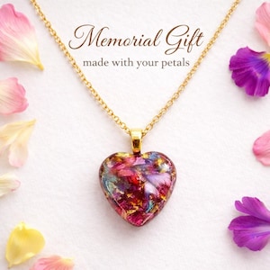 May include: A heart-shaped pendant necklace with a gold chain. The pendant is filled with colorful petals and gold flakes. The text "Memorial Gift made with your petals" is displayed above the pendant.