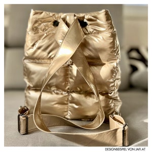 May include: A gold metallic backpack with a quilted design. The bag has adjustable shoulder straps and a drawstring closure. The backpack is made of a shiny, padded material and has a rectangular shape. The bag is shown from the back.