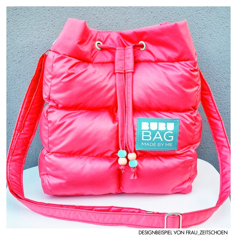 May include: A vibrant pink quilted shoulder bag with a drawstring closure and a long strap. The bag has a rectangular label with the text "BUBU BAG MADE BY ME". The drawstring has decorative beads.