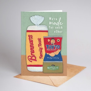 May include: A greeting card with illustrations of a loaf of Brennans Family Toast and a bag of Tayto Cheese & Onion crisps. The card has the text "We're made for each other" on a green background, with a brown envelope.