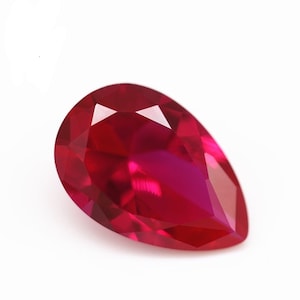 Puede incluir: Una piedra preciosa de color rojo intenso en forma de pera con un corte facetado.