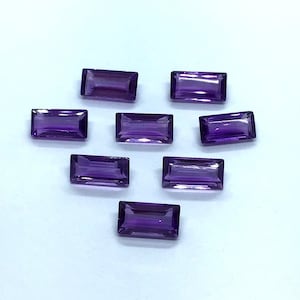 May include: Eight purple amethyst gemstones cut in a rectangular shape.