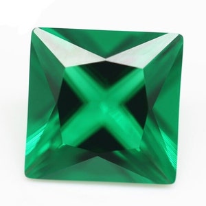 May include: A square-cut, emerald-green gemstone with a faceted surface. The gem has a cross-shaped pattern in the centre, reflecting light. The edges are sharp and well-defined, showcasing the gem's clarity and brilliance. The gemstone is set against a white background.