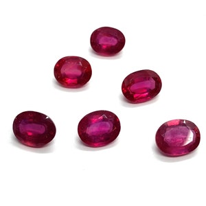 Op de afbeelding: Zes ovale, dieprode edelstenen. De edelstenen zijn gefacetteerd en hebben een gepolijste afwerking.