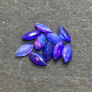 May include: A group of eight marquise-shaped blue opal gemstones with iridescent purple and blue hues.