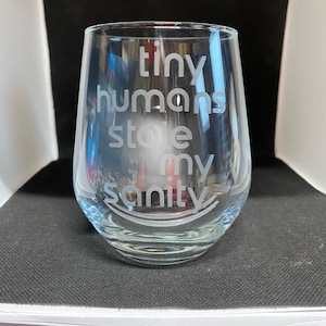 May include: A clear glass wine glass with the text "tiny humans stole my sanity" etched on the side.