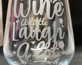 May include: A clear glass wine glass with the text "wine a little laugh a lot" etched into the side.
