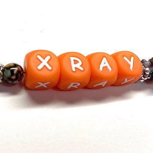 May include: Orange letter beads spelling out the word "XRAY" on a beaded bracelet. The beads are orange with white letters.