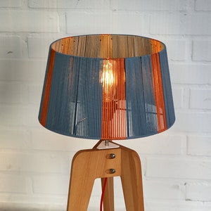 May include: A wooden tripod lamp with a blue and orange striped lampshade. The lamp has a red cord and a white switch.
