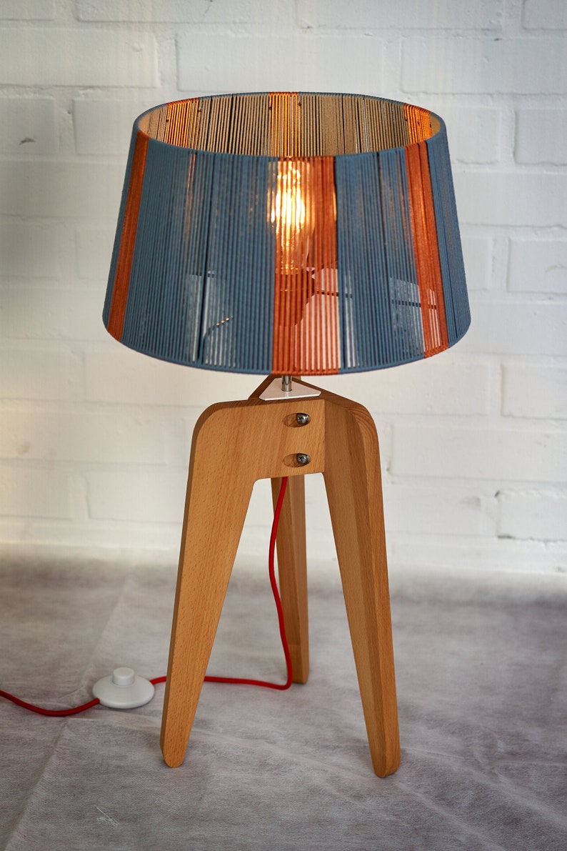 May include: A wooden tripod lamp with a blue and orange striped lampshade. The lamp has a red cord and a white switch.