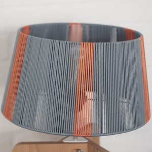 May include: A gray and orange lampshade made of woven cord, with a wooden base.
