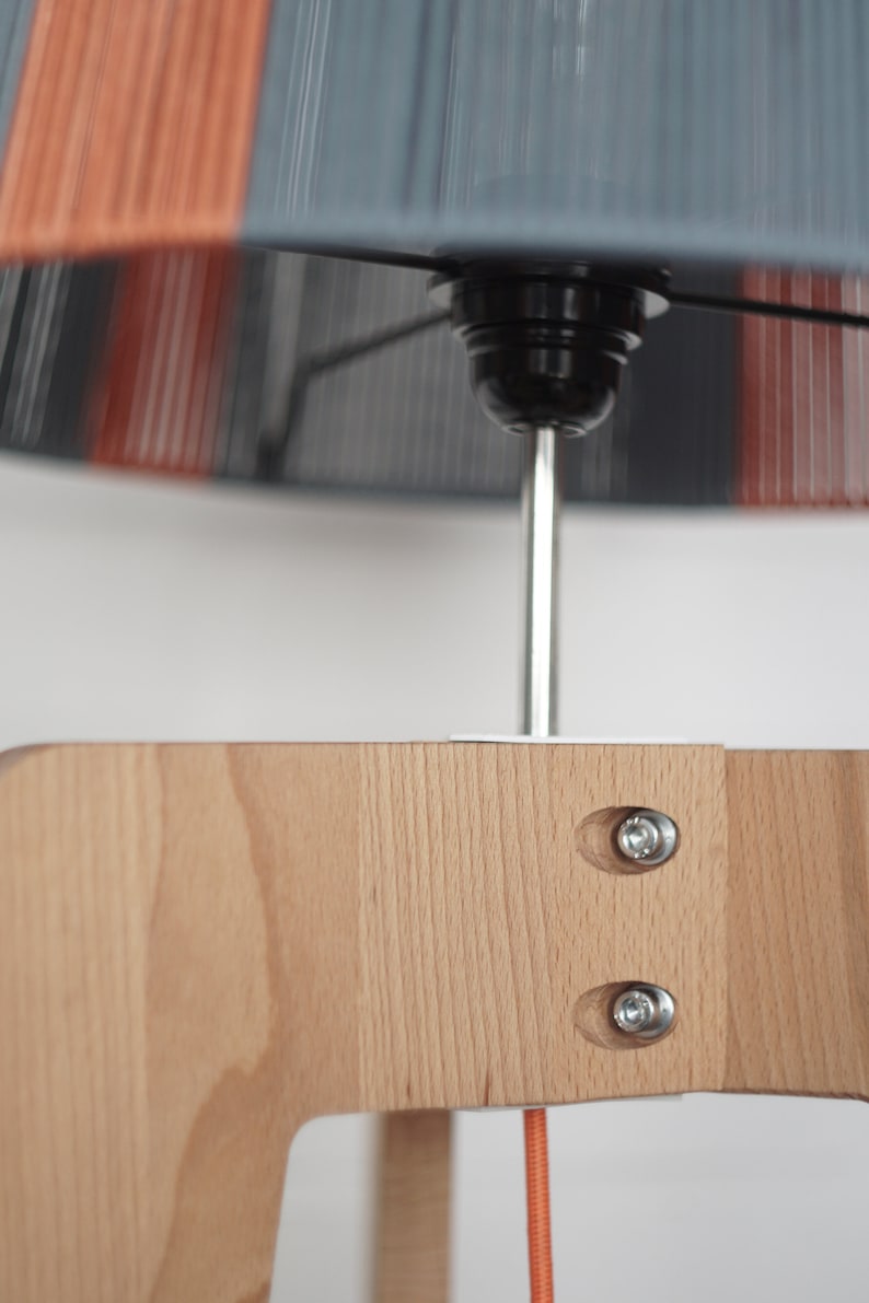 May include: A wooden lamp base with a gray and orange lampshade. The lampshade is attached to the base with a metal rod and screws. The lampshade has a striped pattern.