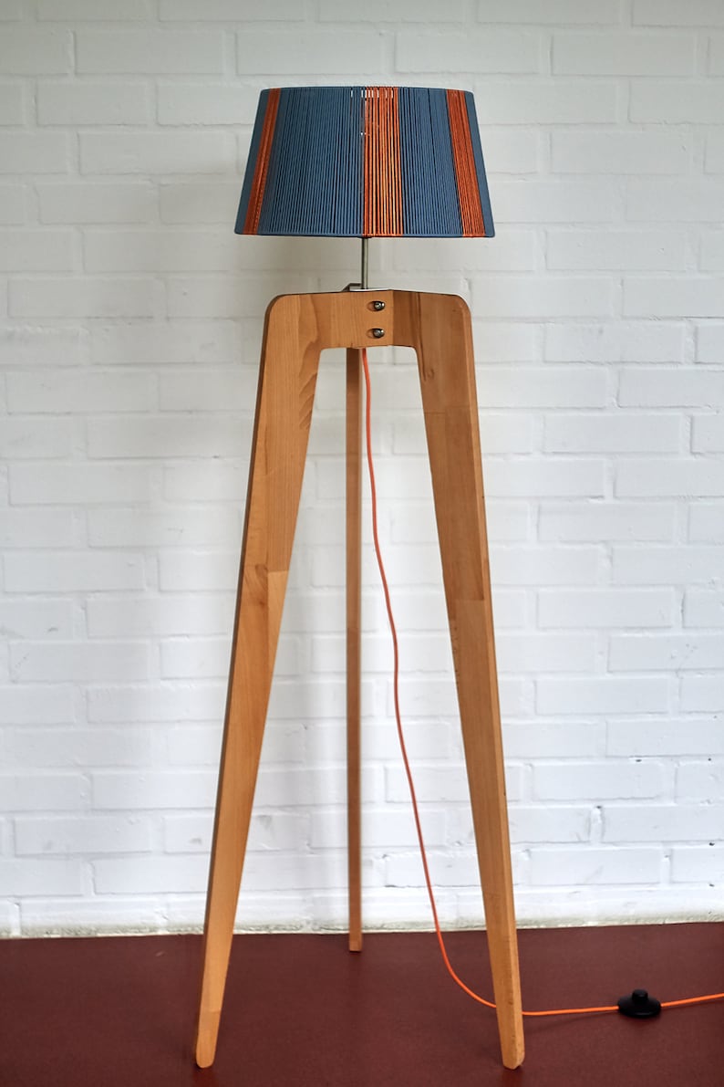 May include: A wooden tripod floor lamp with a blue and orange striped lampshade. The lamp has a long orange cord with a black switch.