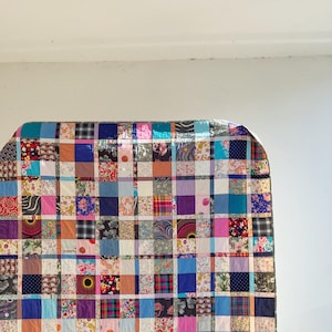 May include: A large patchwork quilt made from a variety of colorful fabrics. The quilt is made up of squares of different colors and patterns, including floral, geometric, and plaid. The quilt is a vibrant and eclectic piece of textile art.