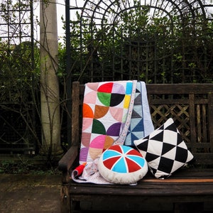 Peut inclure: Un banc en bois avec une courtepointe géométrique colorée, un coussin à motifs noir et blanc et un coussin rond à rayures rouges, bleues et blanches.