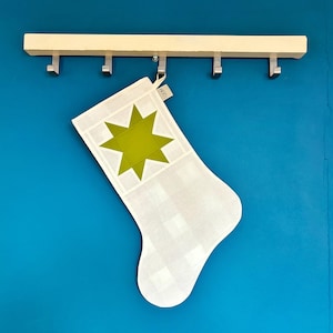 K&ouml;nnte beinhalten: Ein wei&szlig;-hellgrau karierter Weihnachtsstrumpf mit einem gro&szlig;en, einfarbigen, lindgr&uuml;nen achtstrahligen Stern in der Mitte des Umschlags. Ein kleines wei&szlig;es Stoffetikett mit dem Text LOOM ist an der oberen Schlaufe des Strumpfes befestigt.