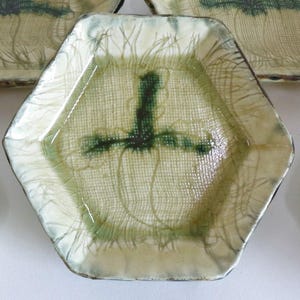 Könnte beinhalten: Satz von sechs sechseckigen Keramiktellern mit einem grün-weißen Design. Die Teller haben eine strukturierte Oberfläche und einen erhöhten Rand.