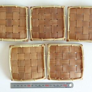Puede incluir: Cinco posavasos cuadrados de bamb&uacute; tejido de color marr&oacute;n claro con un borde beige claro.