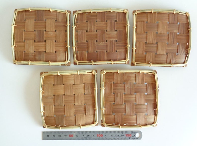 Puede incluir: Cinco posavasos cuadrados de bamb&uacute; tejido de color marr&oacute;n claro con un borde beige claro.