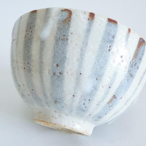May include: A ceramic bowl with a white and gray striped pattern. The bowl has a rounded shape with a small, slightly flared base. The stripes are vertical and evenly spaced, with small brown speckles throughout.
