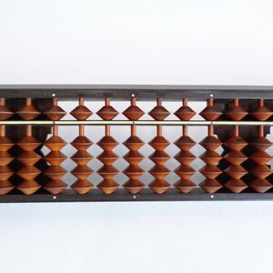 May include: A wooden abacus with brown beads and a dark brown frame. The abacus has two rows of beads, each with 17 beads.