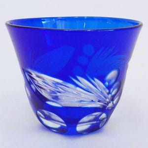 Puede incluir: Una taza de vidrio azul cobalto con un diseño de vidrio cortado. La taza es transparente por dentro y tiene un aspecto esmerilado.