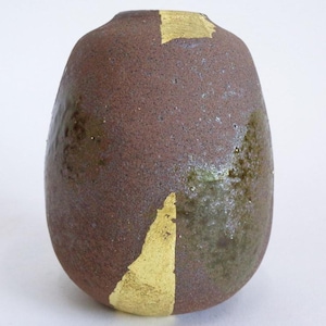 Peut inclure: Un vase artisanal en céramique marron, de forme organique unique. Le vase présente des accents de feuilles d'or sur sa surface, ajoutant une touche d'élégance. Le vase a une surface texturée et une finition légèrement brillante.