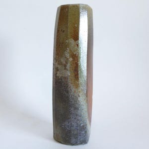 Peut inclure: Un vase en céramique de forme rectangulaire et à surface texturée. Il présente des rayures verticales dans les tons marron, vert et rouge. Le design a un aspect rustique et artisanal, adapté à la décoration intérieure.
