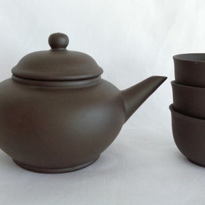 以下が含まれることがあります： 蓋と3つの小さなカップがセットになった、茶色の陶器製のティーポット。ティーポットは丸いボディと湾曲したハンドルを持っています。