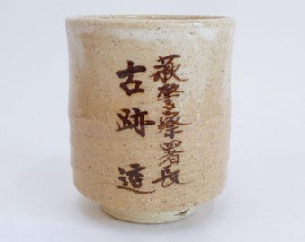 Puede incluir: Una taza de té de cerámica marrón claro con una inscripción marrón oscuro que dice "古渡  酒蔵".