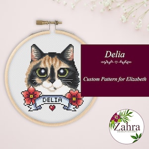 Könnte beinhalten: Eine Kreuzstich-Stickerei eines Katzenkopfes mit schwarzem, braunem und weißem Fell. Das Design beinhaltet ein Banner mit dem Namen "DELIA" und roten Blumen. Der Text "Custom Pattern for Elizabeth" ist ebenfalls vorhanden.